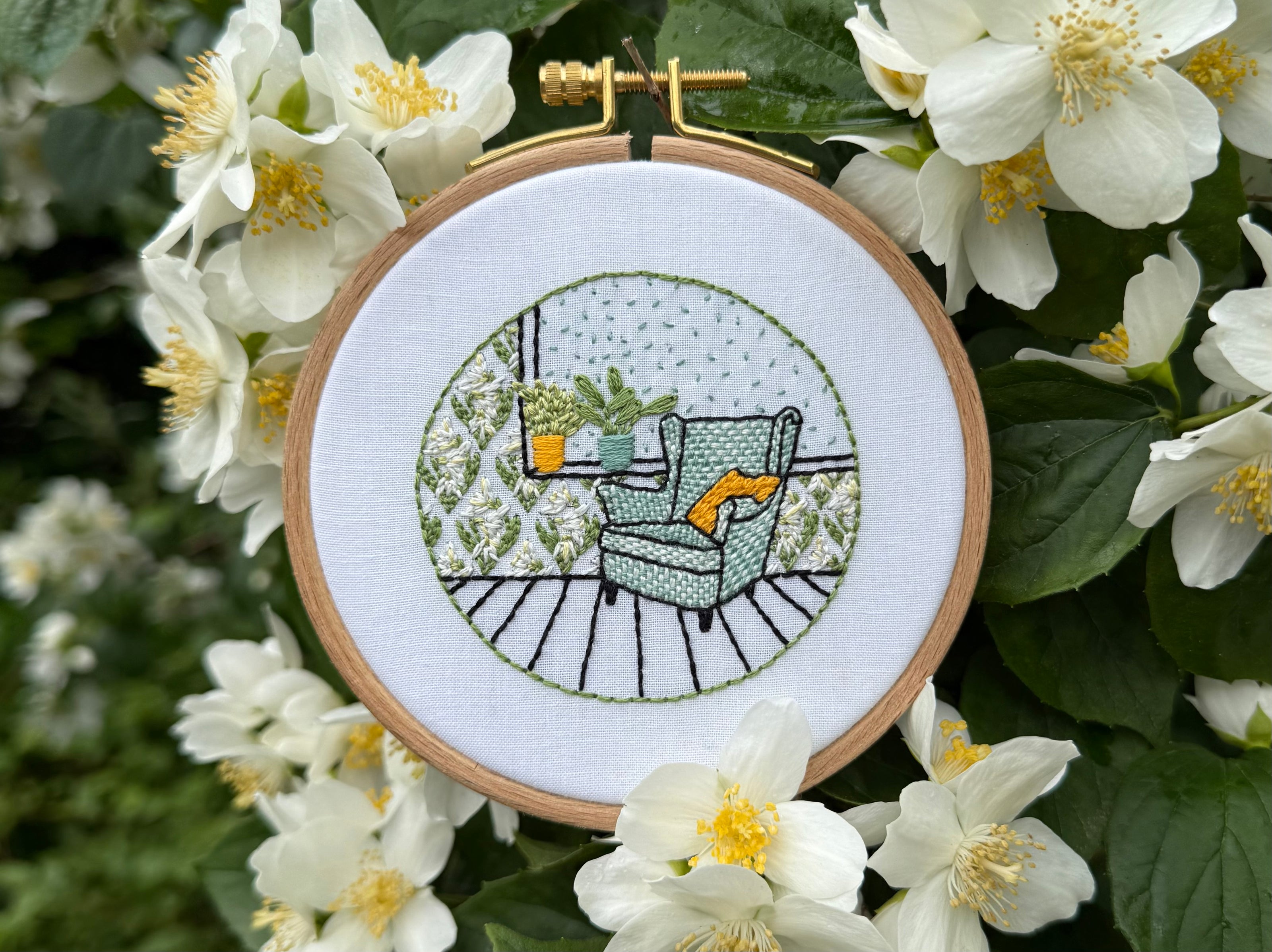 Embroidery hoop with a nature-themed design surrounded by white flowers